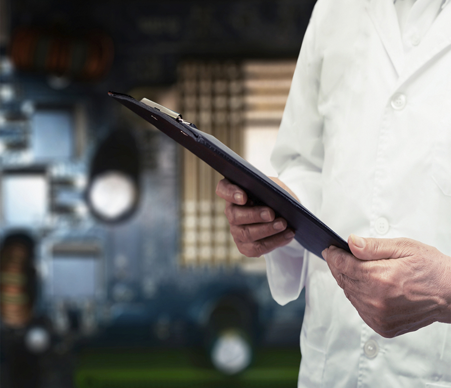 A person wearing a white lab coat is holding a clipboard, partially visible from the waist down. The background is blurry and features various laboratory equipment and instruments.